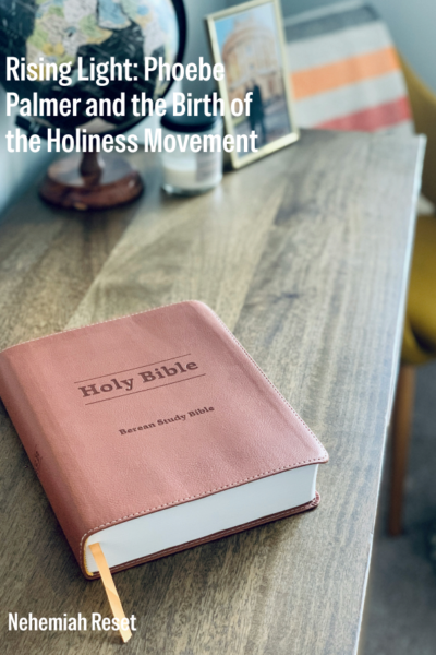Book cover with a pink Holy Bible on a wooden desk; globe and framed photo in the background.